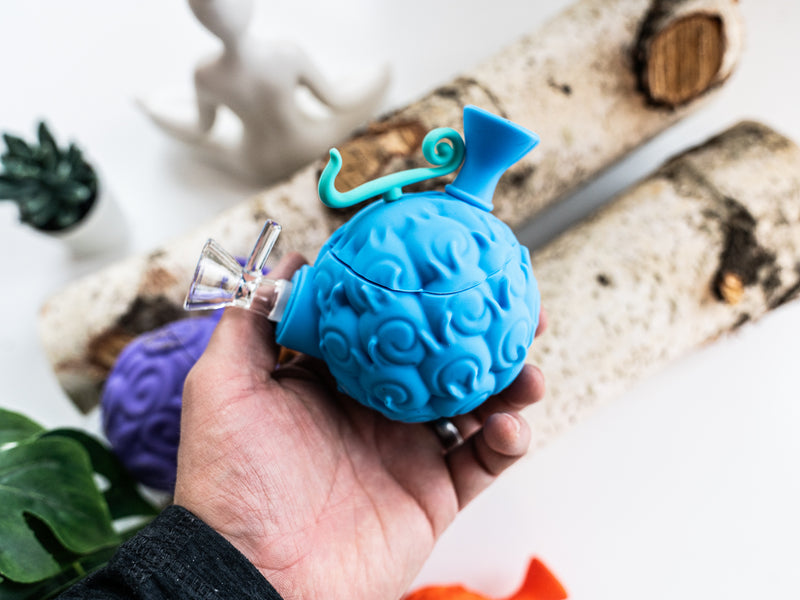 Blue devil fruit silicone water pipe held in one hand with glass bowl and teal mouthpiece